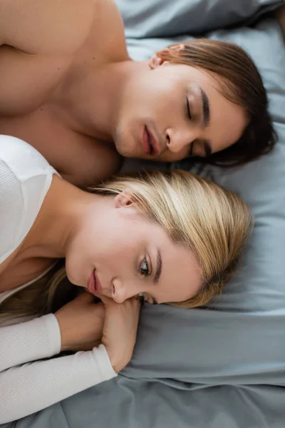 Vista superior de la mujer despierta acostada en la cama con el hombre dormido después de una noche de stand - foto de stock