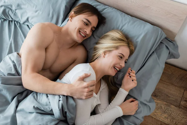 Draufsicht des hemdslosen Mannes, der sich nach einem One-Night-Stand mit blonder Frau umarmt und lacht — Stockfoto