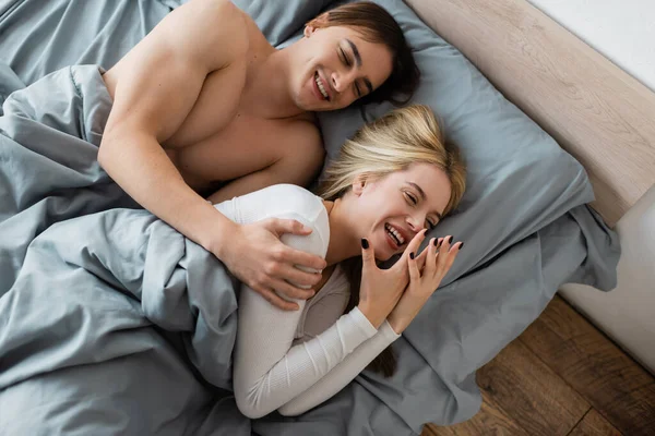 Draufsicht des hemdslosen Mannes, der sich nach einem One-Night-Stand mit einer glücklichen Frau umarmt und lacht — Stockfoto
