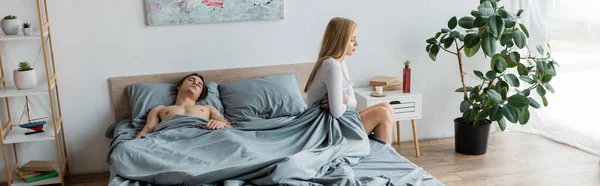 Розчарована жінка сидить на ліжку біля без сорочки після однієї нічної трибуни, банер — стокове фото