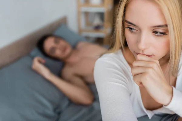 Беспокойная женщина, прикрывающая рот, рядом с размытым мужчиной без рубашки, спящим после одной ночи — стоковое фото