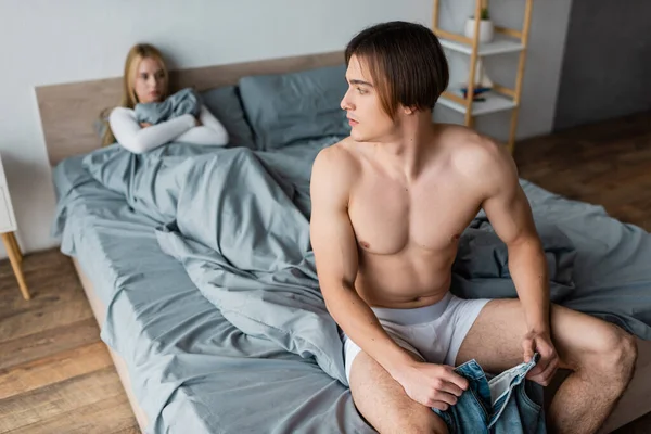 Shirtless man in underwear wearing jeans and looking at woman after one night stand — Stock Photo