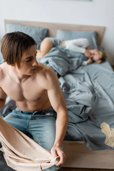 Shirtless man holding clothes after one night stand with blonde woman — Stock Photo