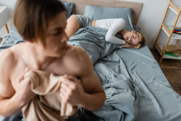 Sad woman regretting of having one night stand with shirtless man on blurred foreground — Stock Photo