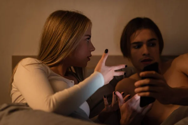 Mujer rubia haciendo gestos mientras discute con su novio por la noche, concepto de engaño - foto de stock