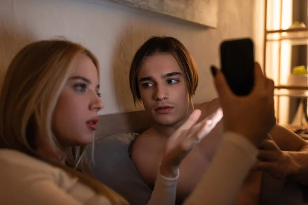 Blondine hält Handy in der Hand, während sie mit Freund im Schlafzimmer streitet, betrügt Konzept — Stockfoto