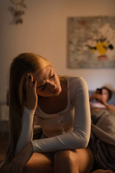 Upset woman sitting on bed near blurred boyfriend in bedroom — Stock Photo