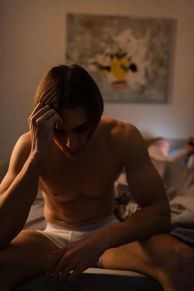 Sconvolto e senza maglietta uomo seduto sul letto vicino fidanzata offuscata, concetto di tradimento — Foto stock