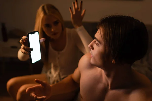 Blonde woman holding smartphone while arguing with unfaithful boyfriend at night — Stock Photo