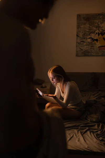 Upset woman reading messages on smartphone near blurred unfaithful boyfriend at night — Stock Photo