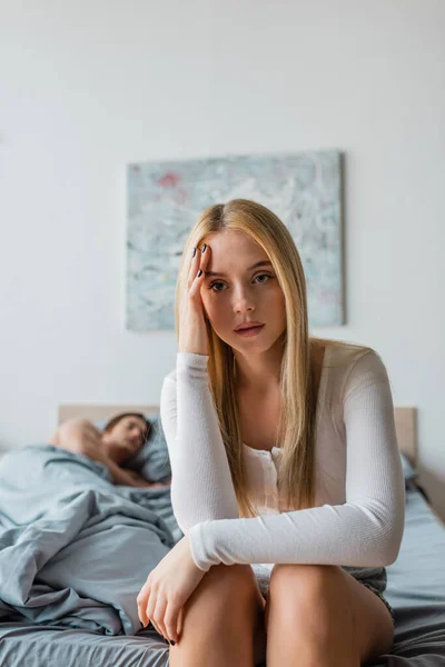 Blonde and worried woman sitting on bed next to man after one night stand — Stock Photo