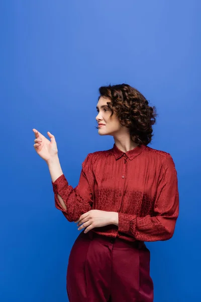 Smiling language teacher with short curly hair gesturing during lesson isolated on blue — Stock Photo