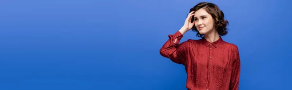 Thoughtful language teacher in red blouse smiling while looking away isolated on blue, banner — Stock Photo