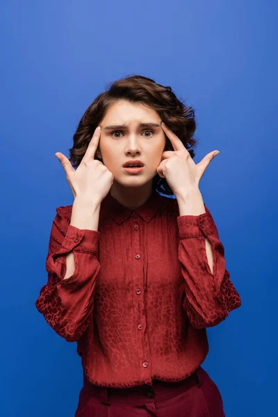 Shocked language teacher with fingers at temples looking at camera isolated on blue — Stock Photo