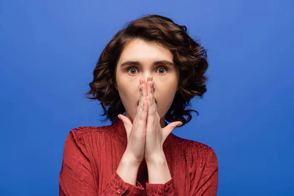 Shocked language tutor covering mouth with hands while looking at camera isolated on blue — Stock Photo