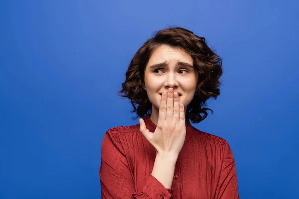 Nervous language teacher covering mouth with hand while looking away isolated on blue — Stock Photo
