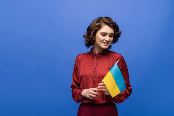 Alegre profesor de idiomas sosteniendo la bandera de Ucrania y sonriendo aislado en azul - foto de stock
