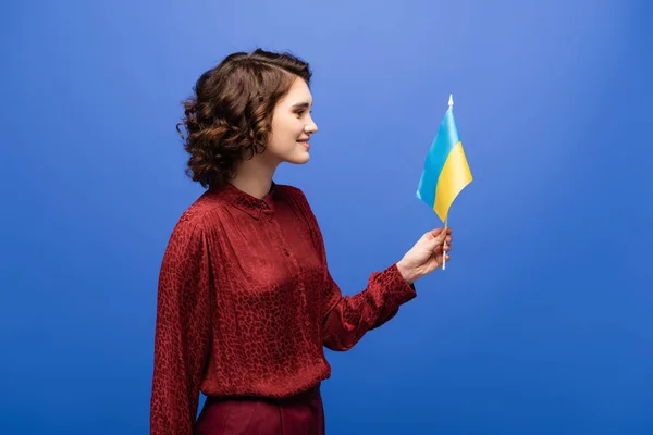 Vue de côté de professeur de langue heureux tenant drapeau de l'Ukraine isolé sur bleu — Photo de stock