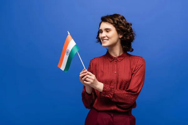 Веселий учитель мови тримає прапор Індії і дивиться на камеру, ізольовану на синьому — стокове фото