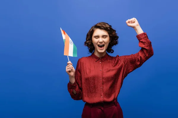 Excited woman with curly short hair holding flag of India isolated on blue — Stock Photo