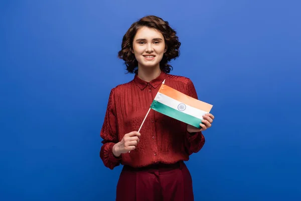 Femme heureuse souriant tout en tenant le drapeau de l'Inde et en regardant la caméra isolée sur bleu — Photo de stock