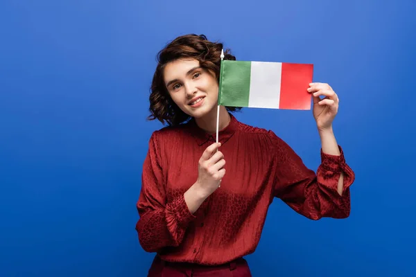 Happy woman smiling while holding flag of Italy and looking at camera isolated on blue — Stock Photo