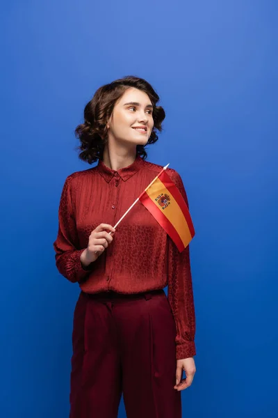 Happy language teacher smiling while holding flag of Spain isolated on blue — Stock Photo