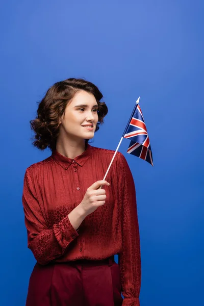 Happy language teacher smiling while looking at flag of United Kingdom isolated on blue — Stock Photo