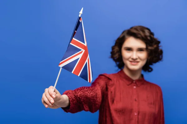 Estudante feliz com cabelo encaracolado olhando para a bandeira do Reino Unido isolado em azul — Fotografia de Stock