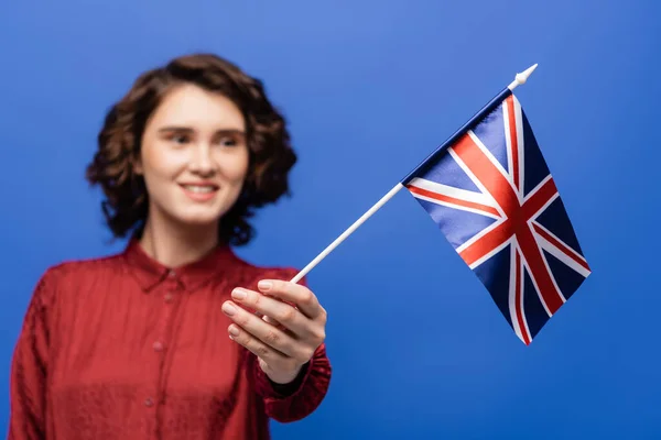 Estudante alegre com cabelo encaracolado olhando para a bandeira do Reino Unido isolado em azul — Fotografia de Stock
