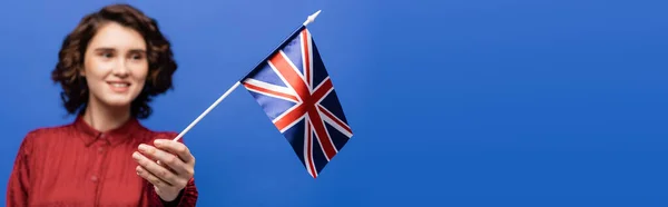 Happy student with curly hair looking at flag of United Kingdom isolated on blue, banner — Stock Photo