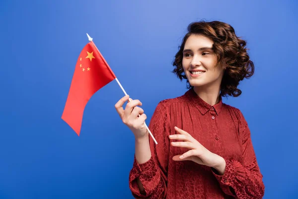 Happy language teacher smiling while holding flag of China isolated on blue — Stock Photo