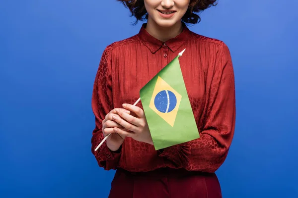 Vista ritagliata di insegnante di lingua felice sorridente mentre tiene la bandiera del Brasile isolata sul blu — Foto stock