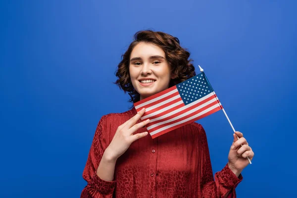 Junge fröhliche Studentin lächelt in die Kamera, während sie die USA-Flagge isoliert auf Blau hält — Stockfoto