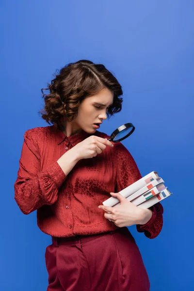 Amazed student looking at textbooks of foreign languages through magnifying glass isolated on blue — Stock Photo