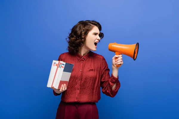 Angry language teacher holding textbooks and screaming in megaphone isolated on blue — Stock Photo