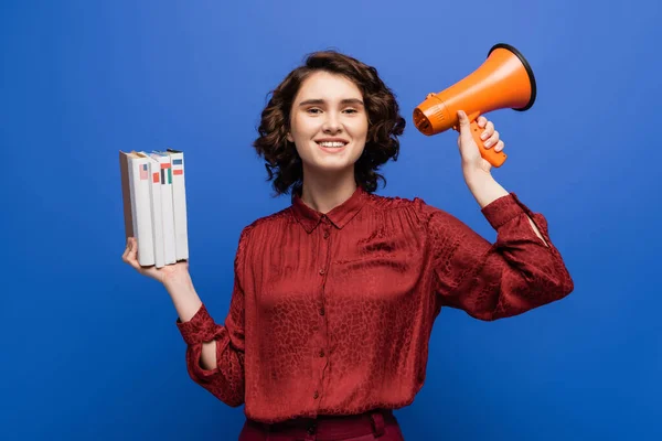 Junge und fröhliche Sprachlehrerin mit Megafon und Schulbüchern auf blauem Grund — Stockfoto