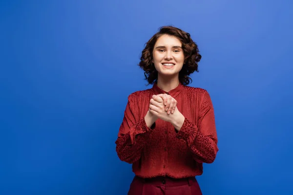 Mujer alegre mostrando gesto que significa amistad en el lenguaje de señas aislado en azul - foto de stock