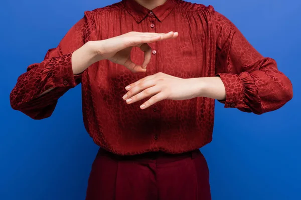 Vista recortada de la mujer en blusa roja hablando en lenguaje de señas aislado en azul - foto de stock