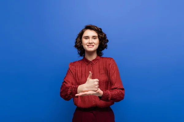 Glückliche Frau lächelt in die Kamera und zeigt Hilfsgeste auf Gebärdensprache isoliert auf blau — Stockfoto