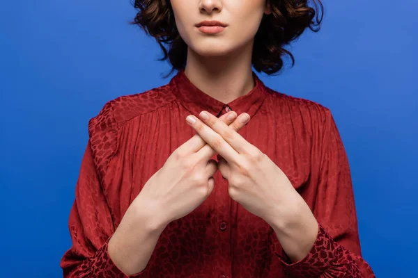 Vista recortada de mujer joven en blusa roja enseñando lenguaje de señas aislado en azul - foto de stock