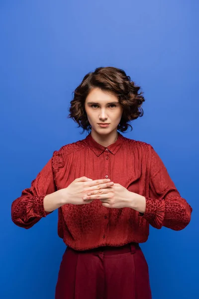 Mujer joven con el pelo rizado mostrando signo que significa nombre en el lenguaje de señas aislado en azul - foto de stock