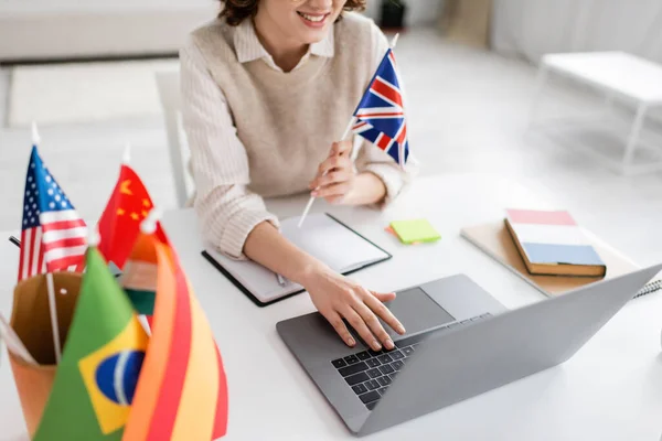 Cropped view of smiling language teacher with flag of United Kingdom using laptop during online lesson at home — Stock Photo