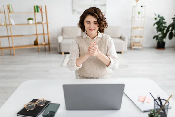 Улыбающаяся женщина показывает жест дружбы при использовании языка жестов во время онлайн-урока на ноутбуке дома — стоковое фото