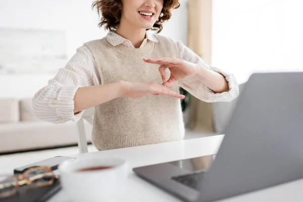 Cropped view of cheerful teacher showing sign language gesture during online lesson on laptop — Stock Photo