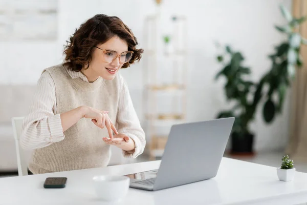 Curly woman showing stand word while teaching sign language during online lesson on laptop — Stock Photo