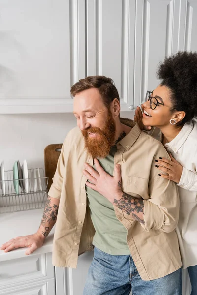 Smiling african american woman talking to bearded boyfriend in kitchen — Stock Photo