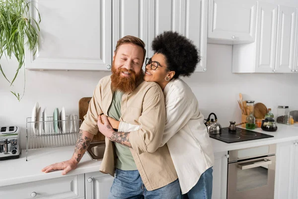 Mulher americana africana alegre abraçando namorado tatuado na cozinha — Fotografia de Stock