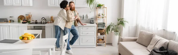 Young african american woman hugging bearded boyfriend in kitchen, banner — Stock Photo