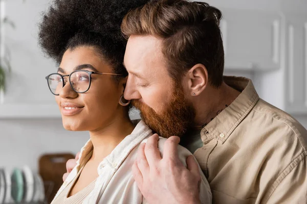 Bearded man hugging smiling african american girlfriend at home — Stock Photo